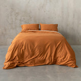 Burnt orange duvet cover set on a bed, against a neutral concrete look backdrop. 