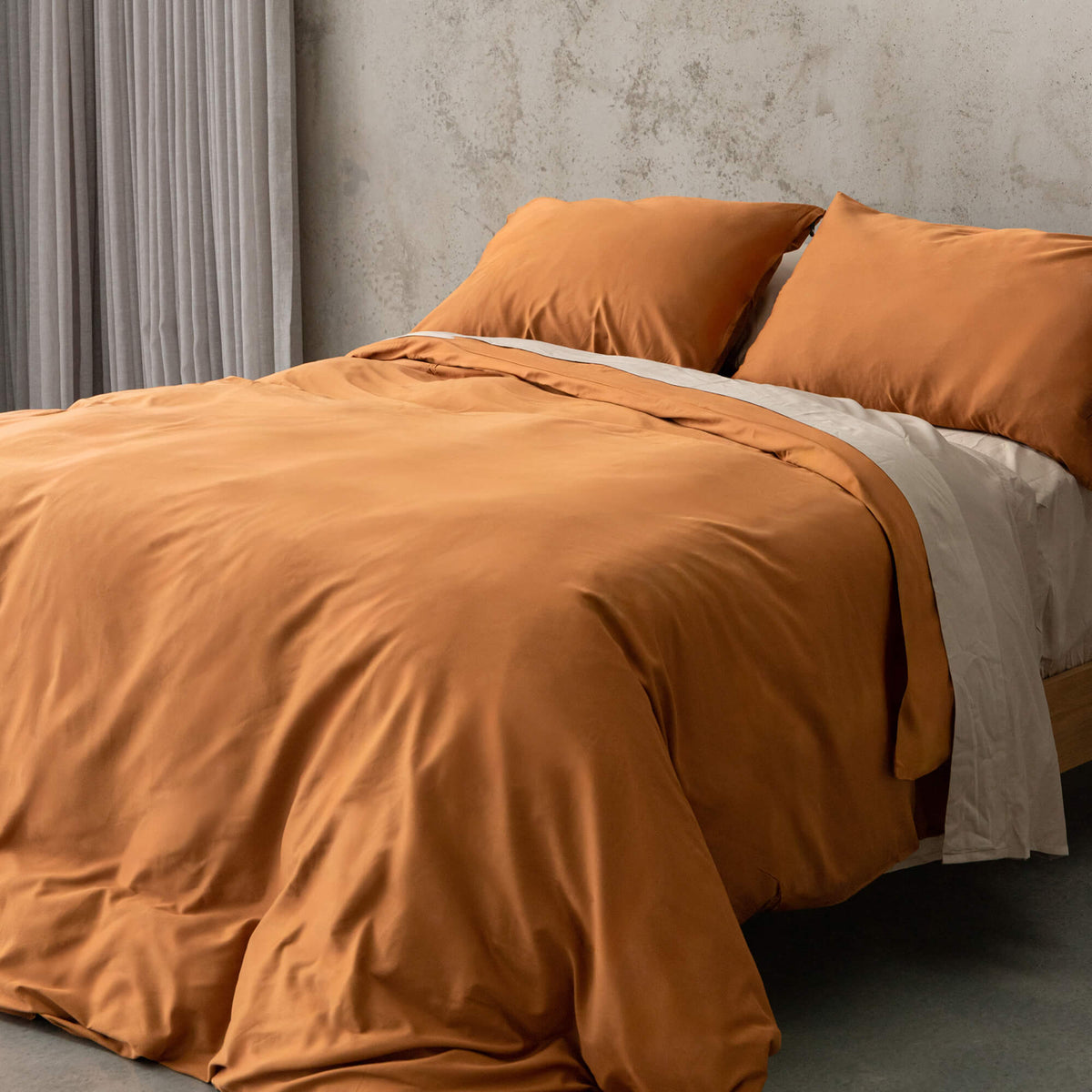 Burnt orange duvet cover set on a bed, against a neutral concrete look backdrop. 