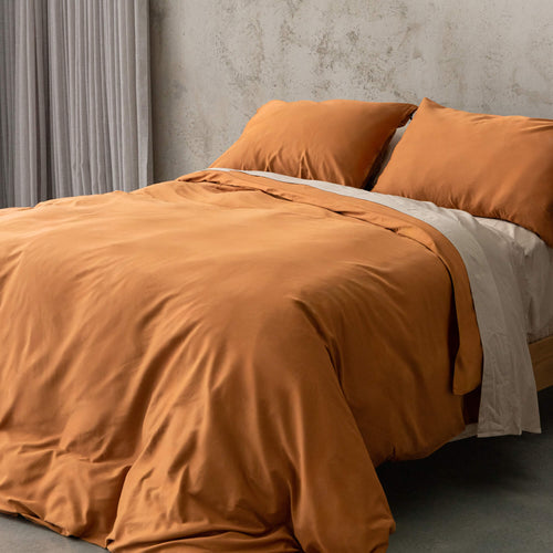 Burnt orange duvet cover set on a bed, against a neutral concrete look backdrop. 