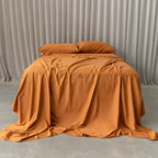 Burnt orange bedding set on a bed, against a neutral backdrop and a beige curtain.