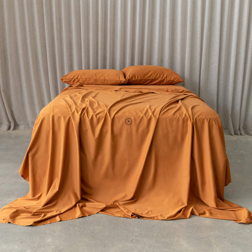 Burnt orange bedding set on a bed, against a neutral backdrop and a beige curtain.