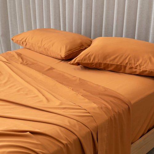 Burnt orange bedding set on a bed, against a neutral backdrop and a beige curtain.