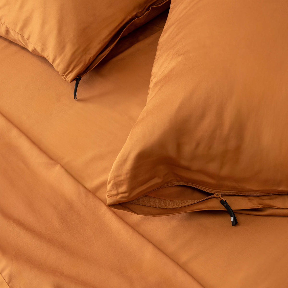 Close-up of two burnt orange pillowcases on a bed with the matching sheets.