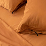 Close-up of two burnt orange pillowcases on a bed with the matching sheets.