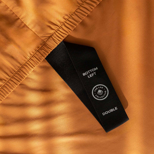 Burnt orange fitted sheet labelled corner loop strap that reads 'Bottom Left' and 'Double'. 