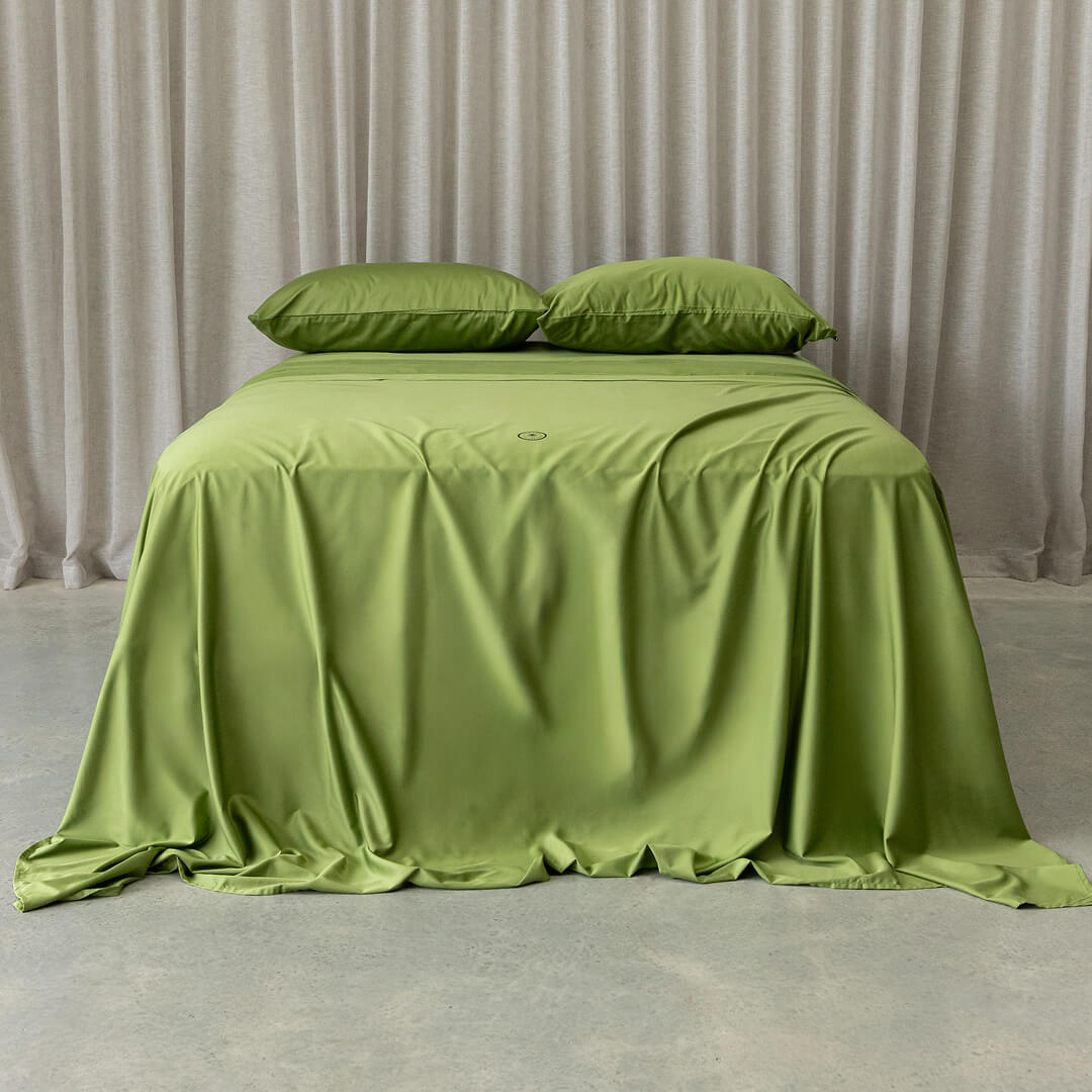 Green bedspread on a bed with matching pillows against a neutral curtain background