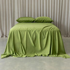 Green bedspread on a bed with matching pillows against a neutral curtain background