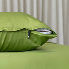 Green pillow with zipper on a bed against a neutral curtain background