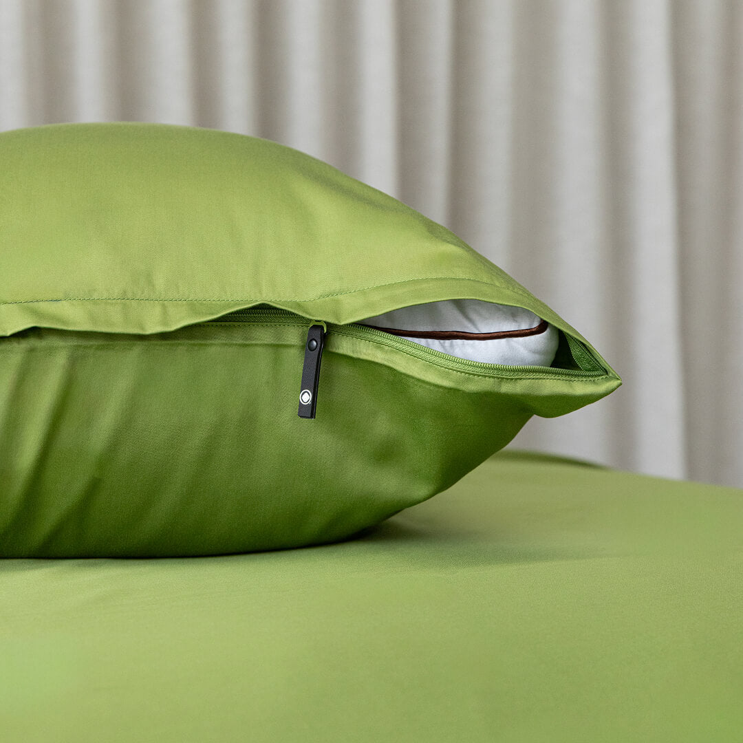 Green pillow with zipper on a bed against a neutral curtain background
