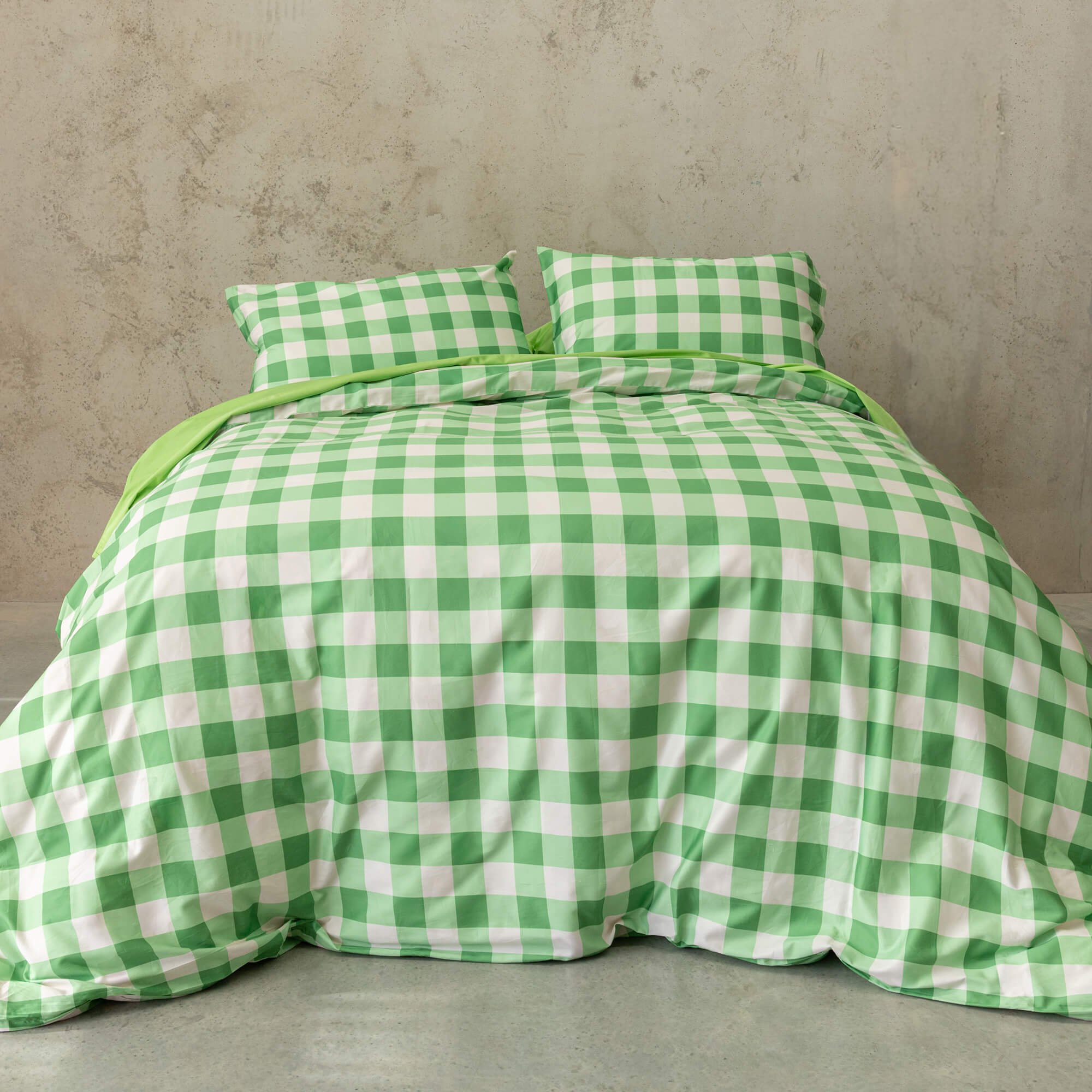 Meadow green gingham print duvet cover set on a bed, against a neutral concrete look backdrop.