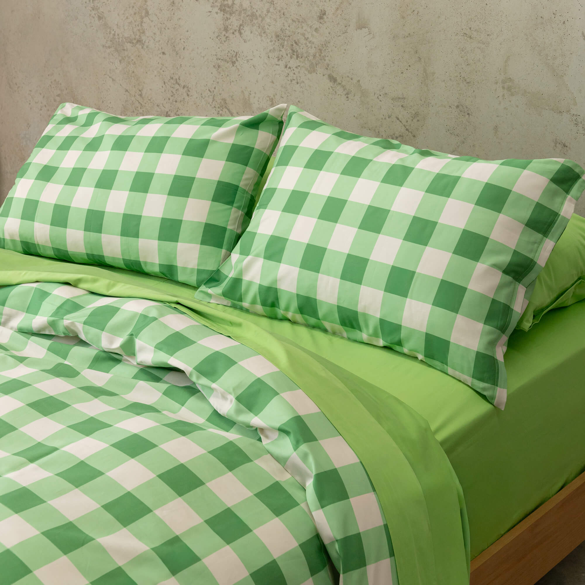 Meadow green gingham print duvet cover set on a bed, against a neutral concrete look backdrop.