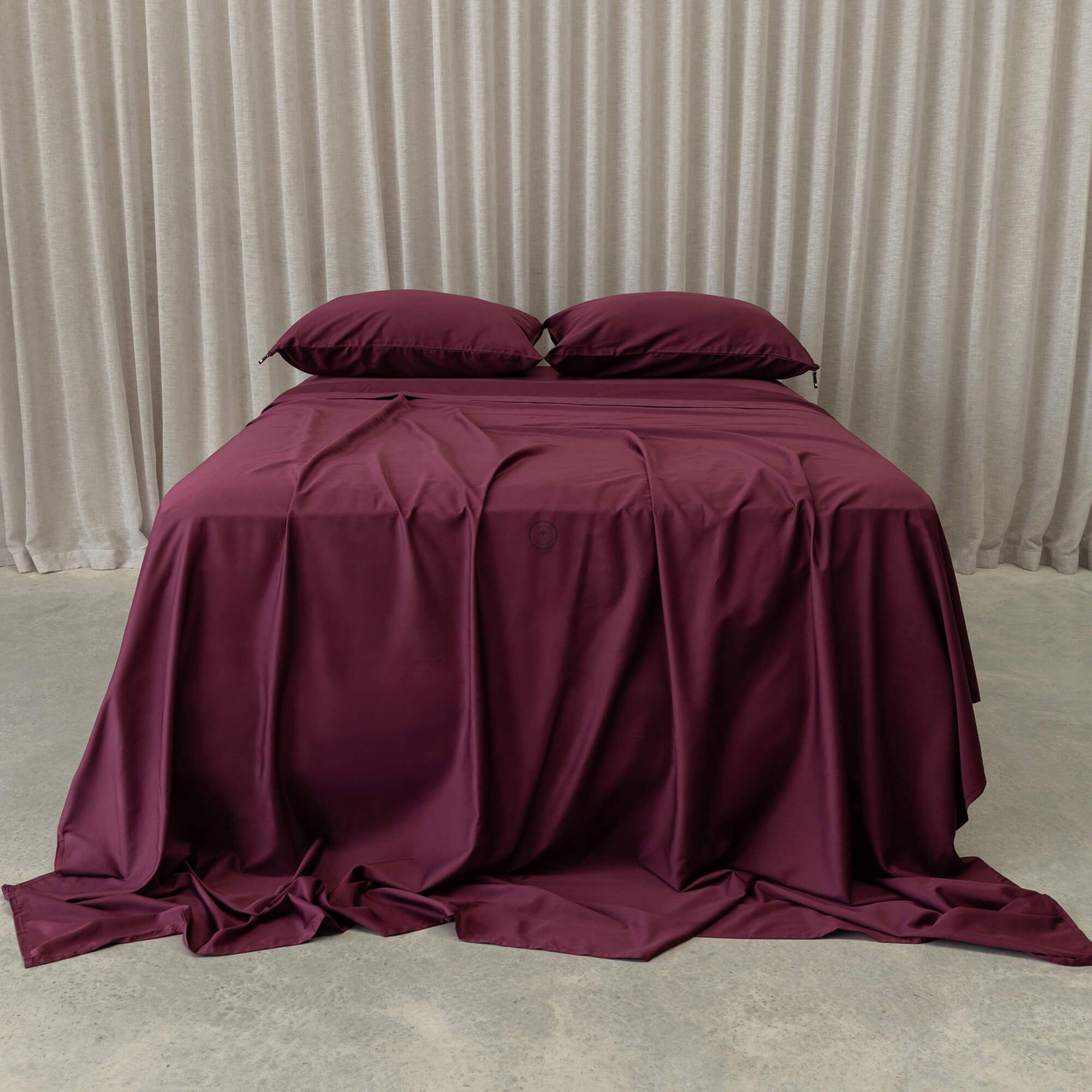 Burgundy bedspread and pillows on a bed against a neutral background
