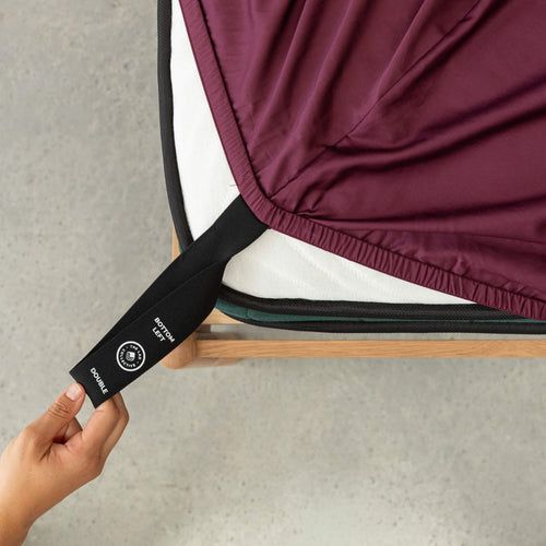 Person holding a black belt with a brand logo over a folded garment on a wooden frame.