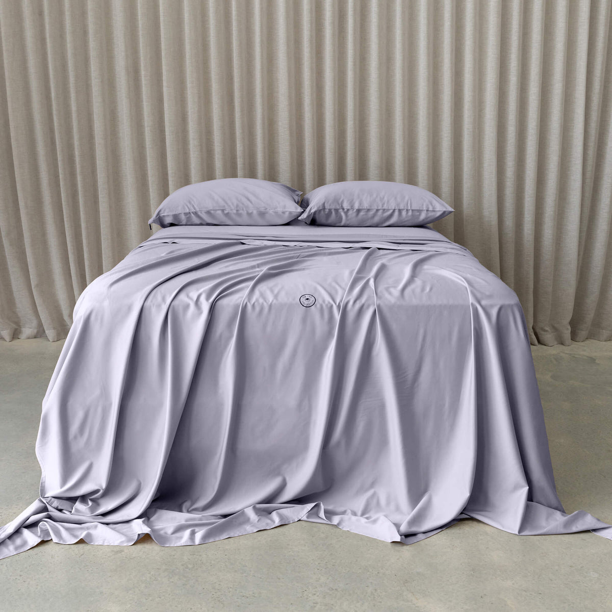 Gray bedspread and pillows on a bed with beige curtains in the background