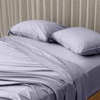 Grey bedspread on a bed with white pillows against a beige curtain background