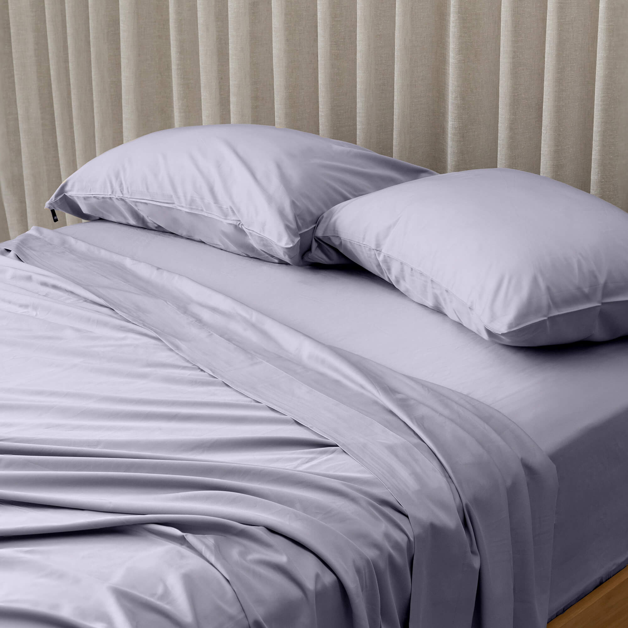 Gray bedspread on a bed with white pillows against a beige curtain background