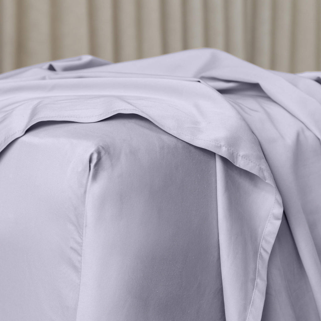 Close up or corner of fitted sheet in gray bedding with sheer curtain background