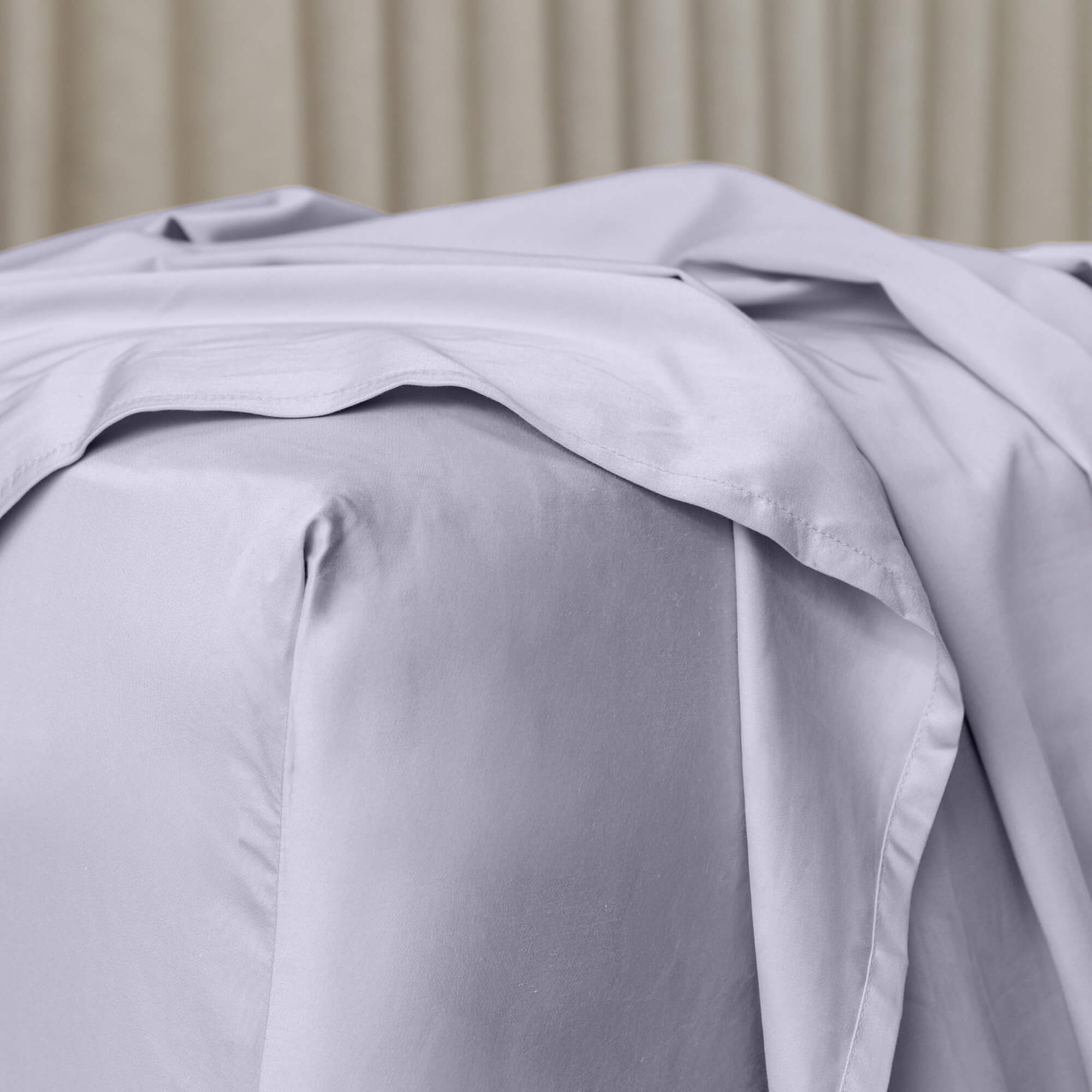 Close up or corner of fitted sheet in gray bedding with sheer curtain background