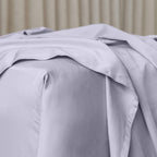 Close up or corner of fitted sheet in gray bedding with sheer curtain background
