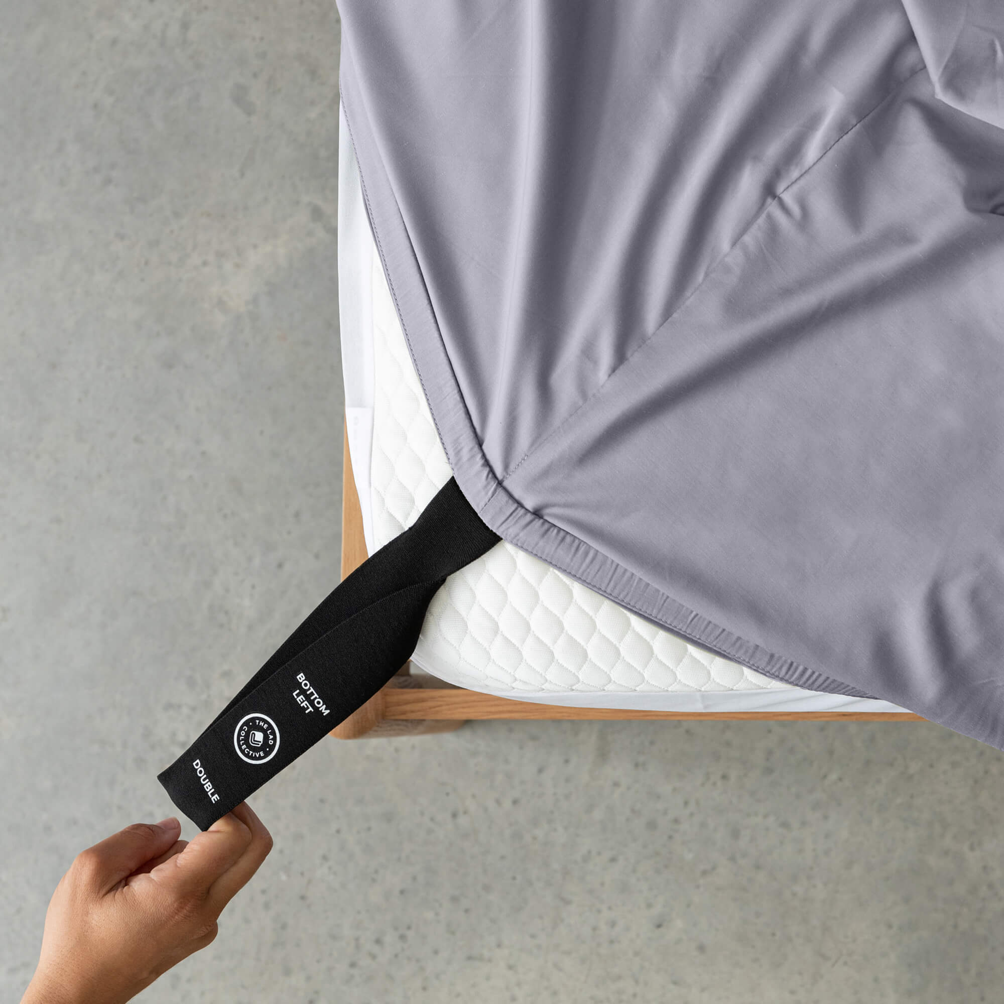 Person adjusting a gray fitted sheet with a black strap on a gray surface