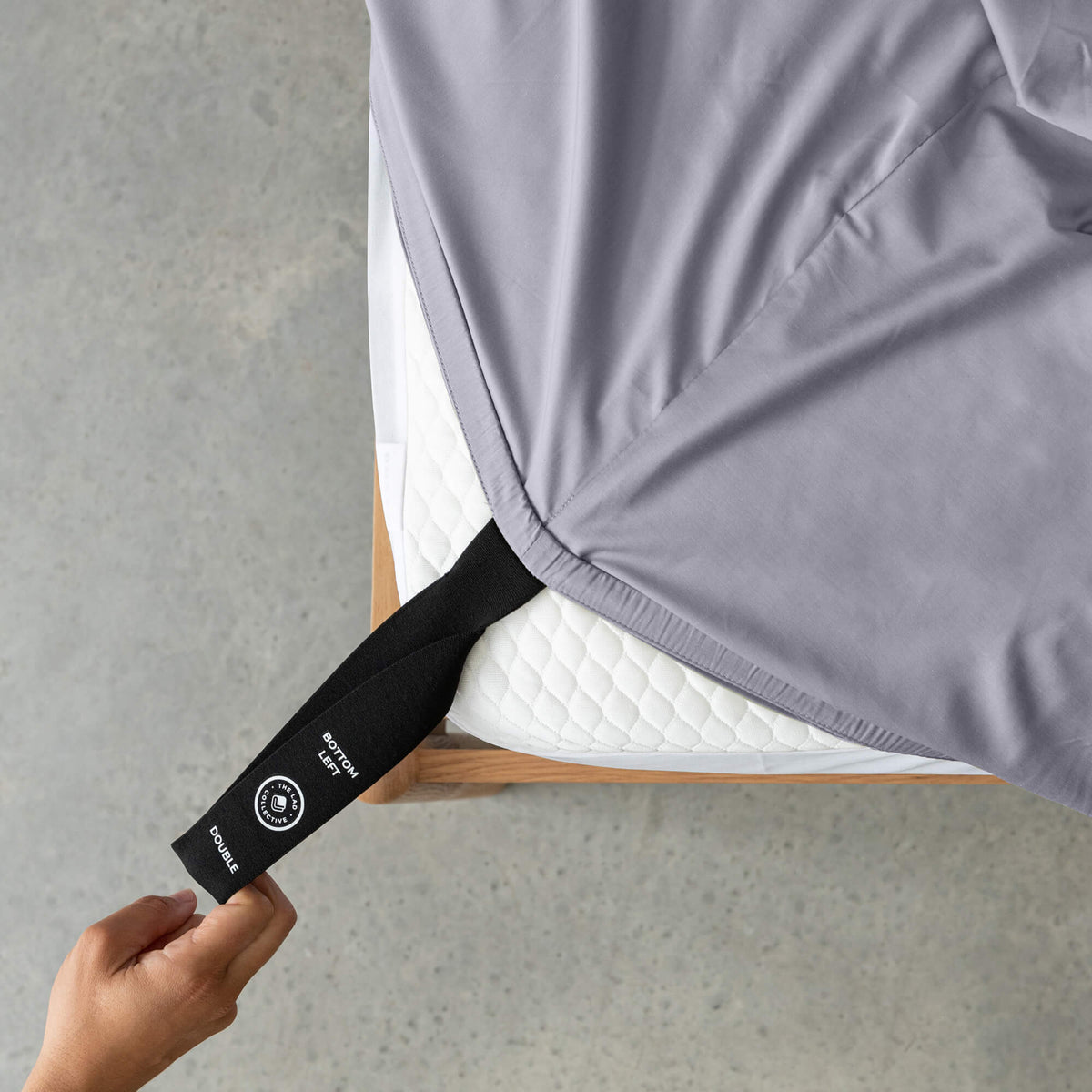 Person adjusting a gray fitted sheet with a black strap on a gray surface