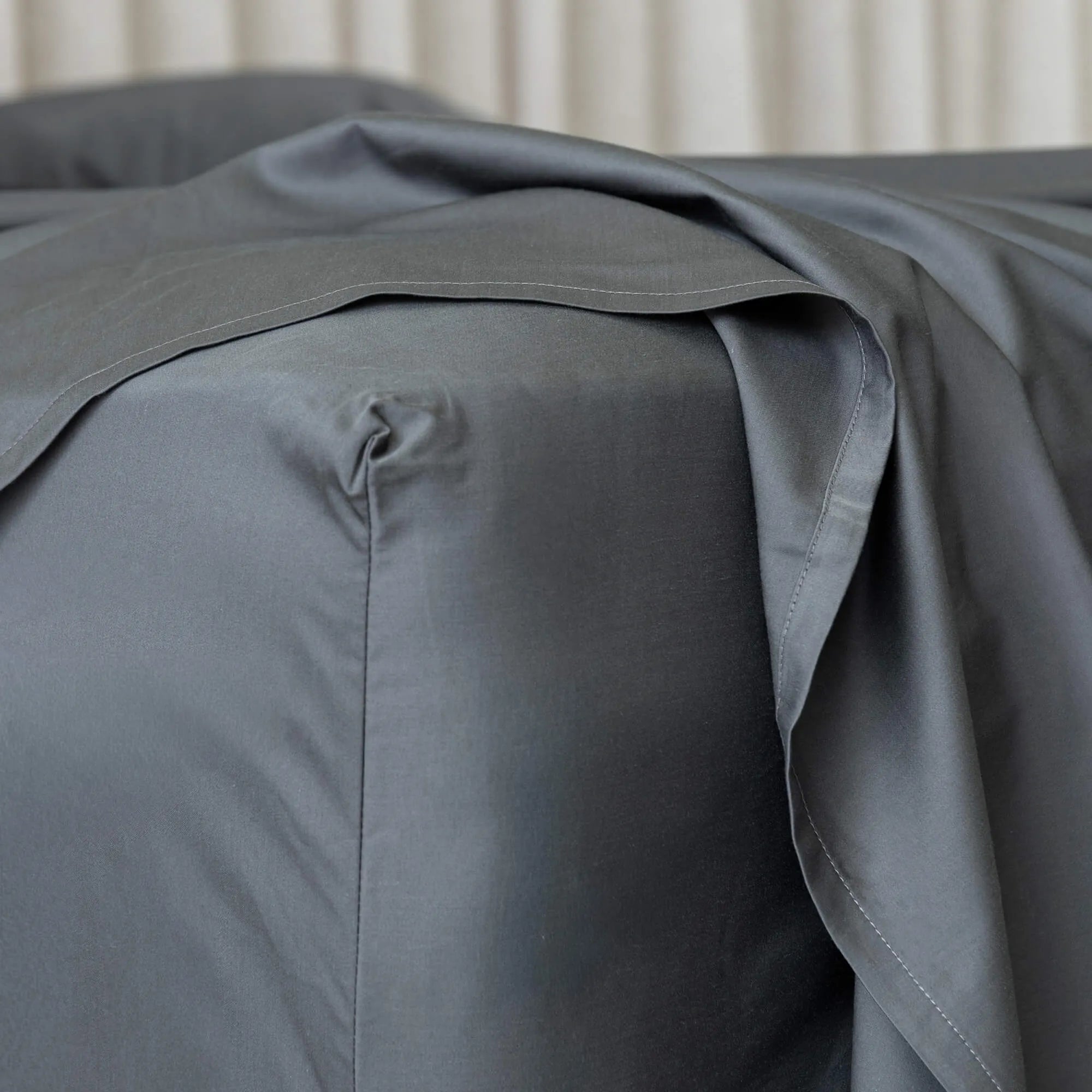 Gray bed sheets on a bed with a neutral background