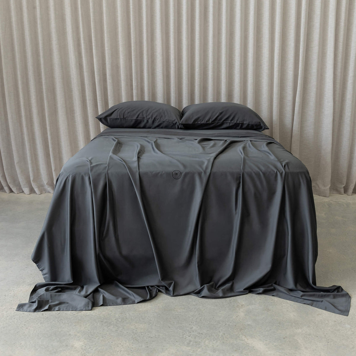 Gray bedspread on a bed with pillows against a beige curtain background.