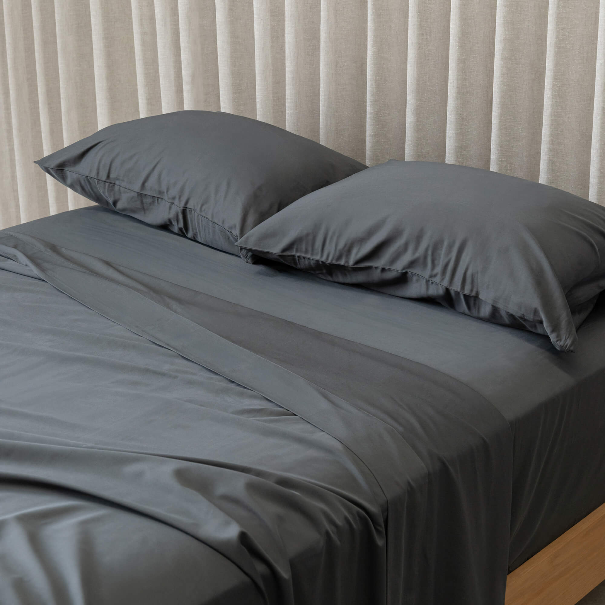 Gray bedspread on a bed with pillows against a beige curtain background.