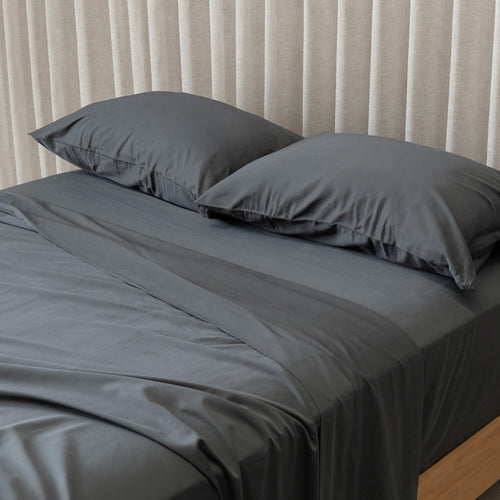 Gray bedspread on a bed with pillows against a beige curtain background.