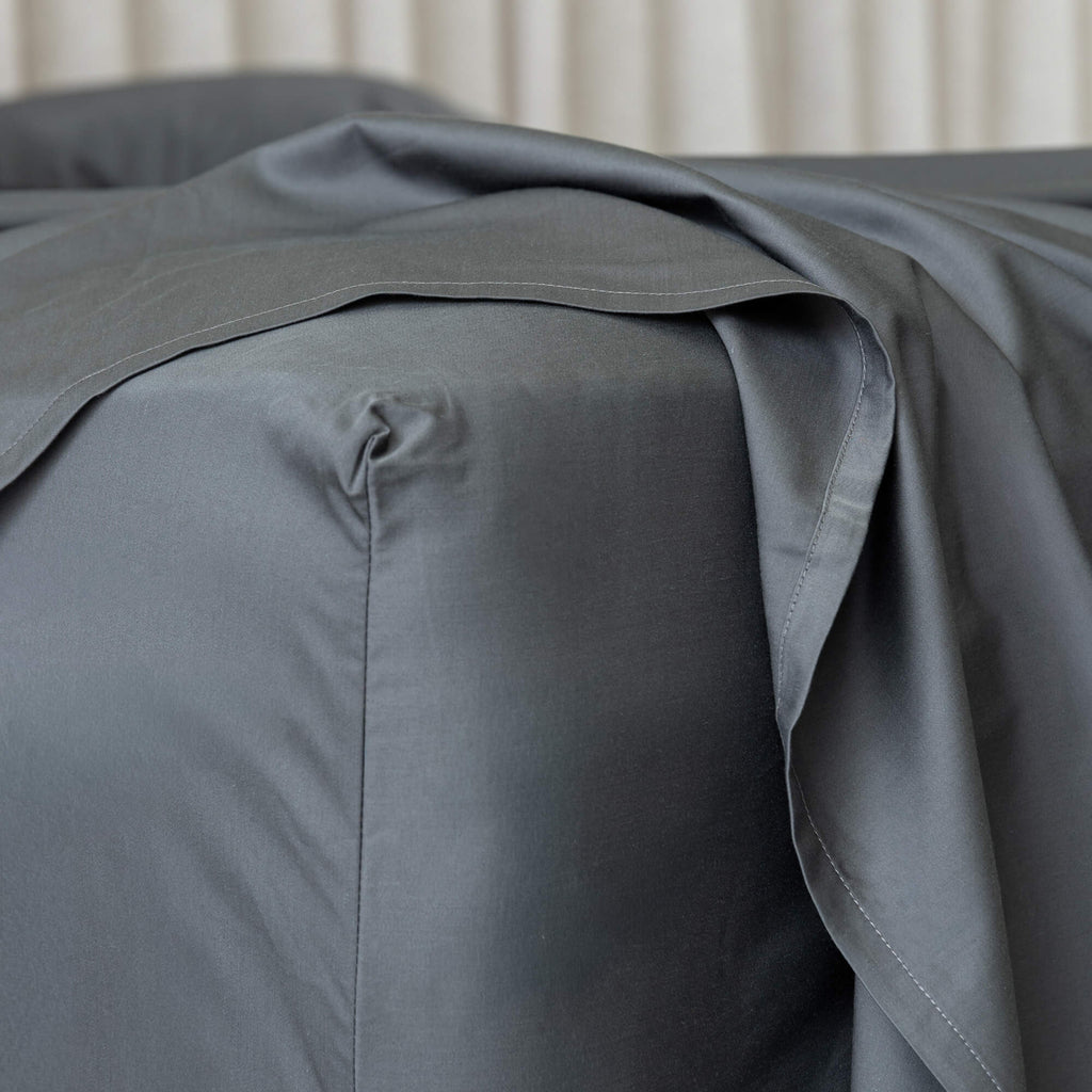 Charcoal gray fitted sheet on a bed, zoomed in on the corner. 
