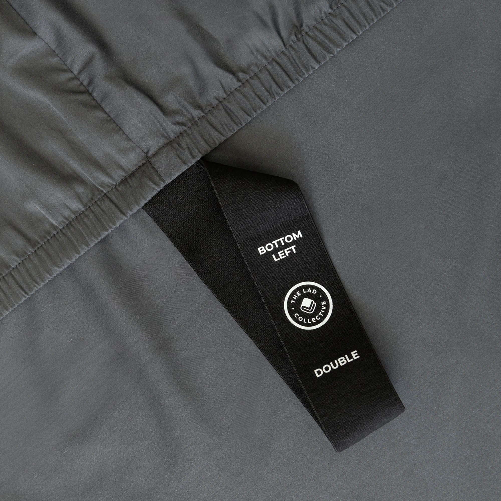 Close-up of a gray fabric with a black labelled loop strap on a matching gray background.