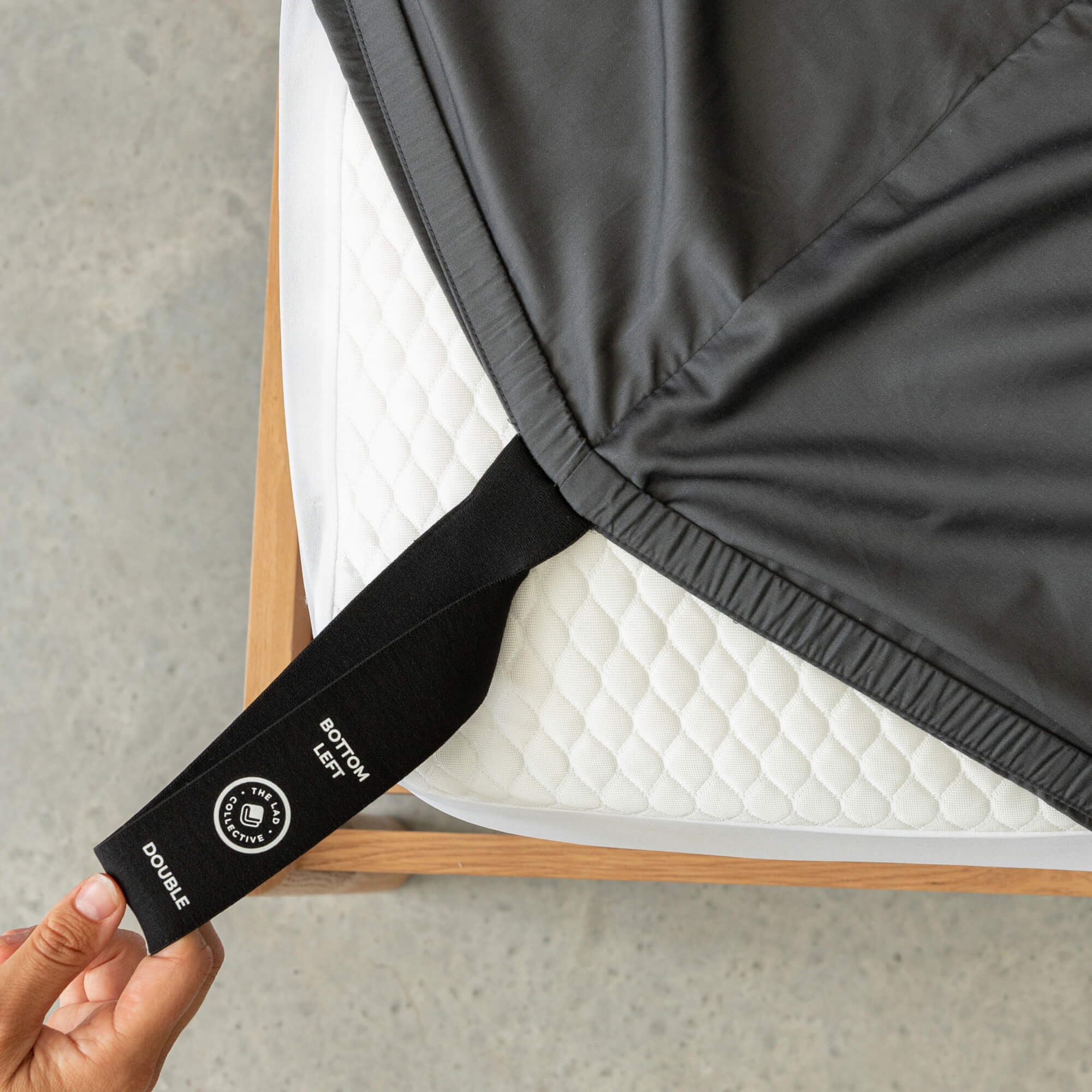 Person holding a black mattress strap labeled 'Bottom Left' and 'Double' on a fitted sheet.