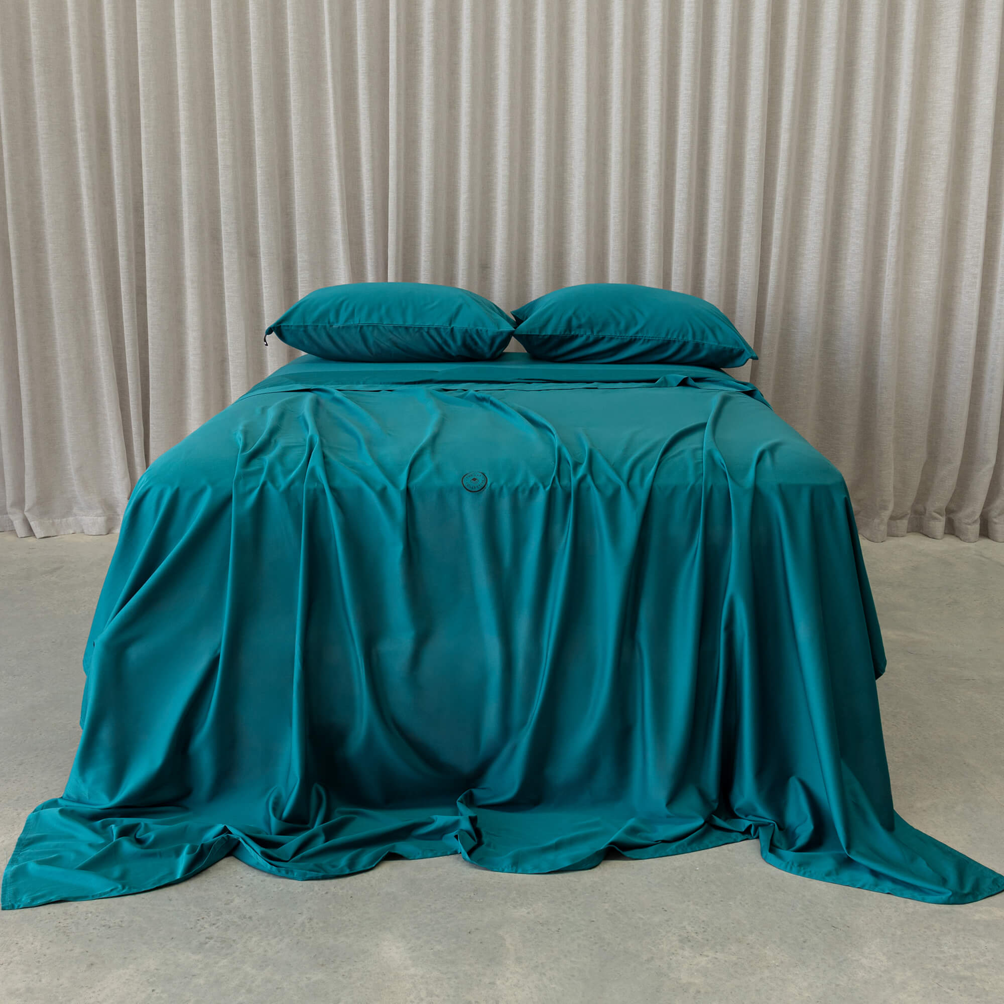 Teal bedspread and pillows on a bed against a beige curtain background