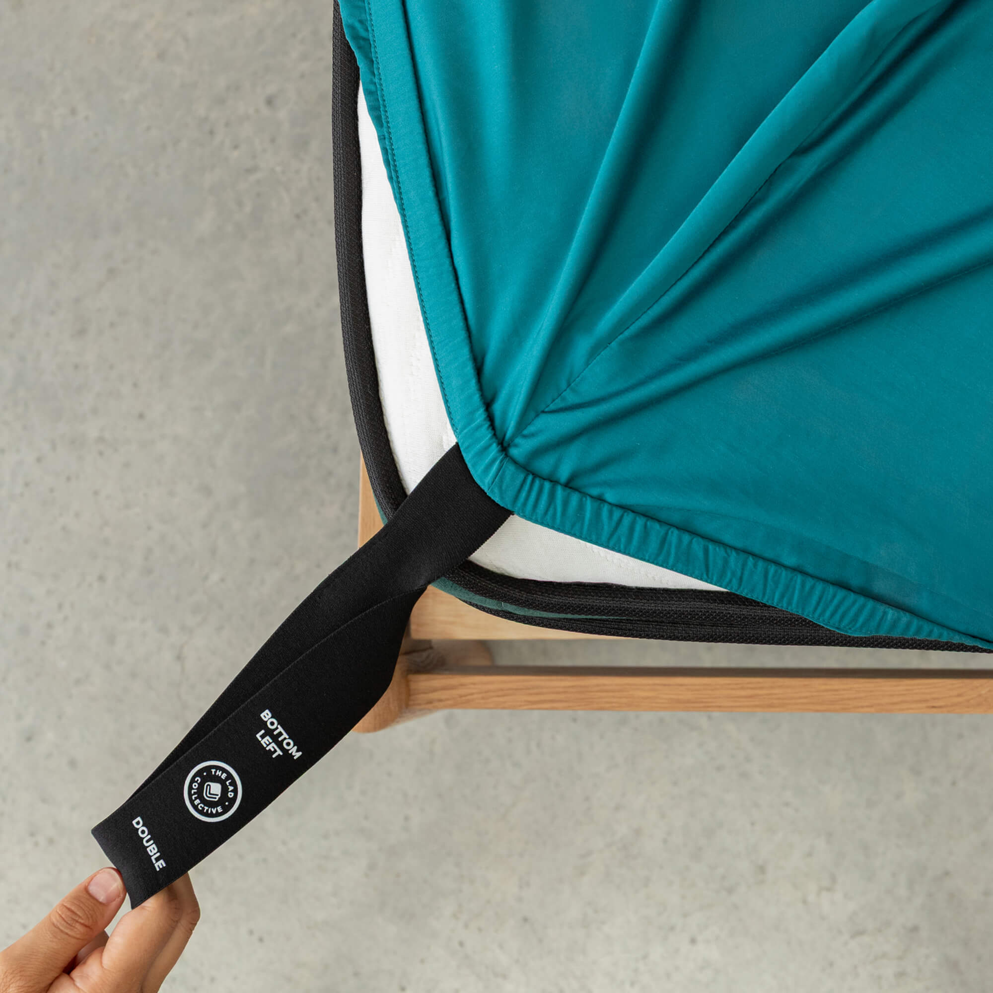 Teal fitted sheet with black strap and visible brand logo on a neutral background