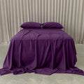 Purple bedspread and pillows on a bed against a beige curtain background