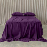 Purple bedspread and pillows on a bed against a beige curtain background