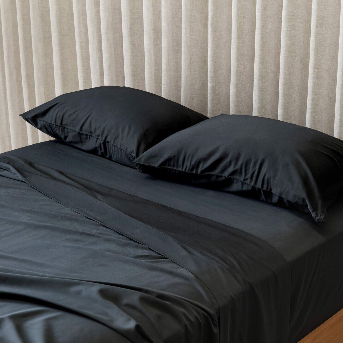 Black bedding set on a bed with light curtains in the background