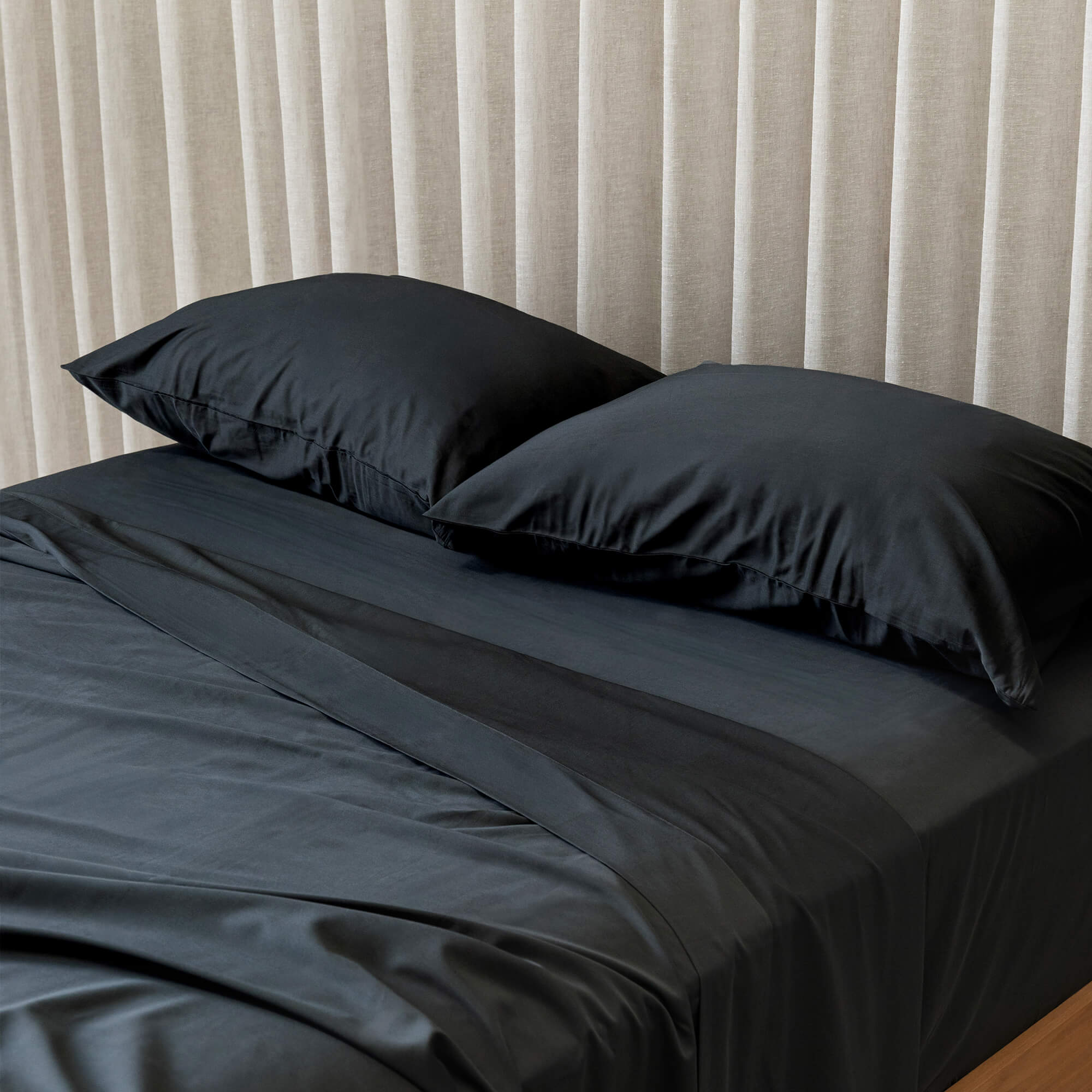 Black bedspread on a bed with pillows against a beige curtain background