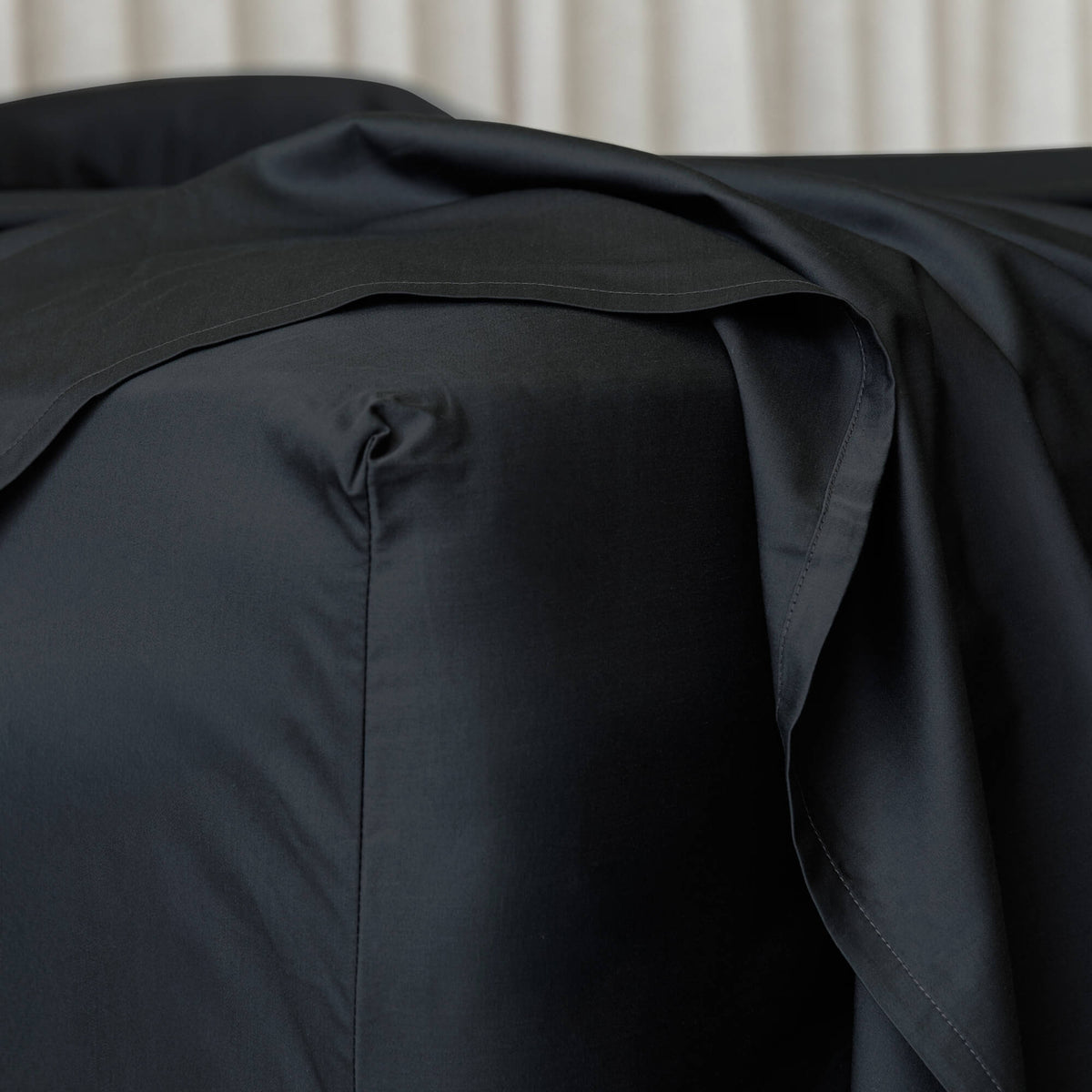 Black bed sheets draped over a bed with a neutral background