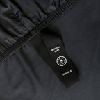 Black bedspread with black corner label on a bed with a neutral background