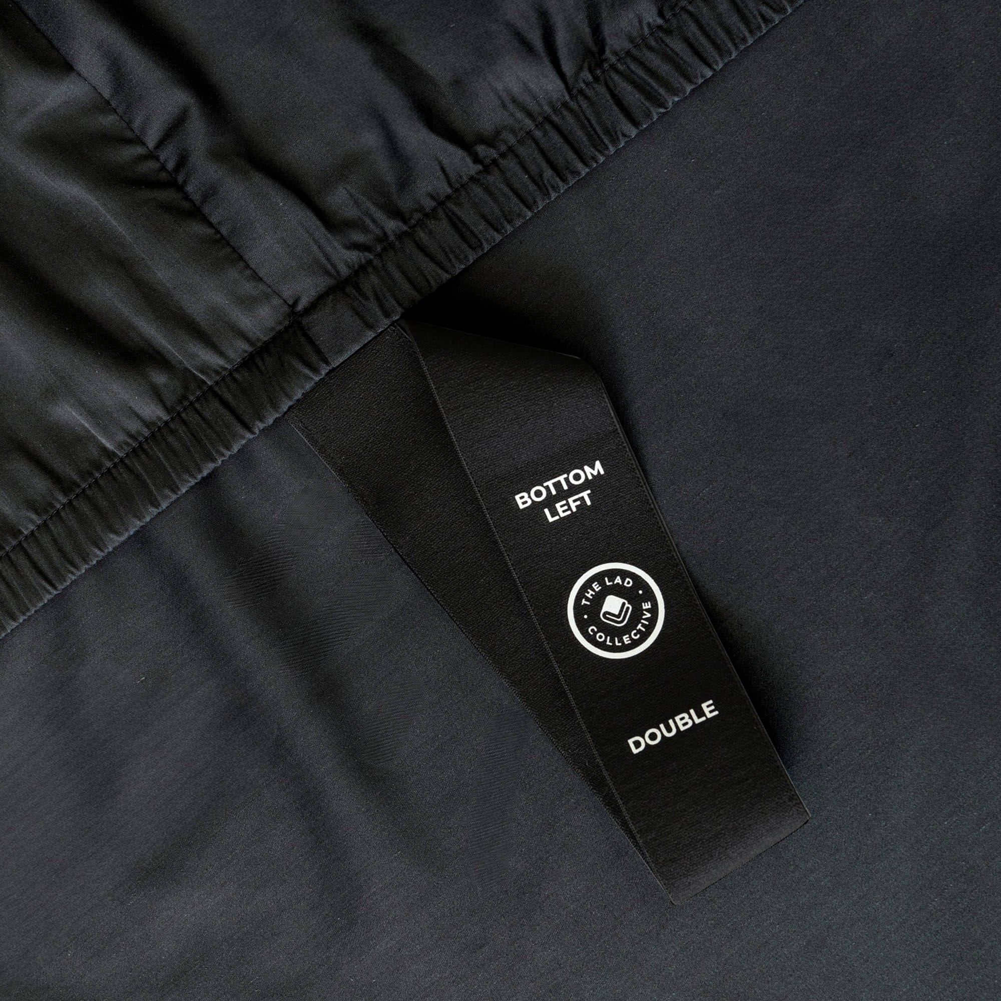 Black bedspread with black corner label on a bed with a neutral background