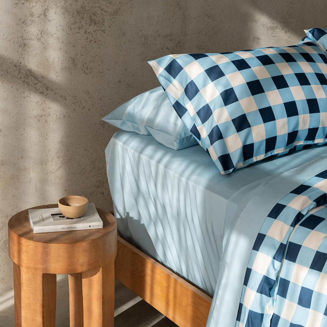 Bed with blue checkered bedding next to a wooden side table.