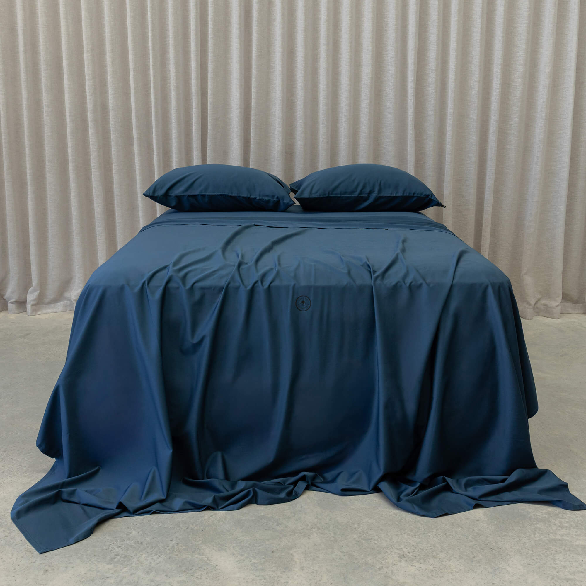Blue bedspread on a bed with pillows against a neutral background