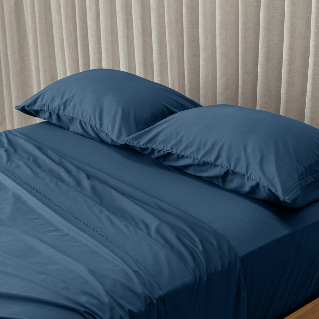 Navy Blue bedspread on a bed with pillows against a beige curtain background