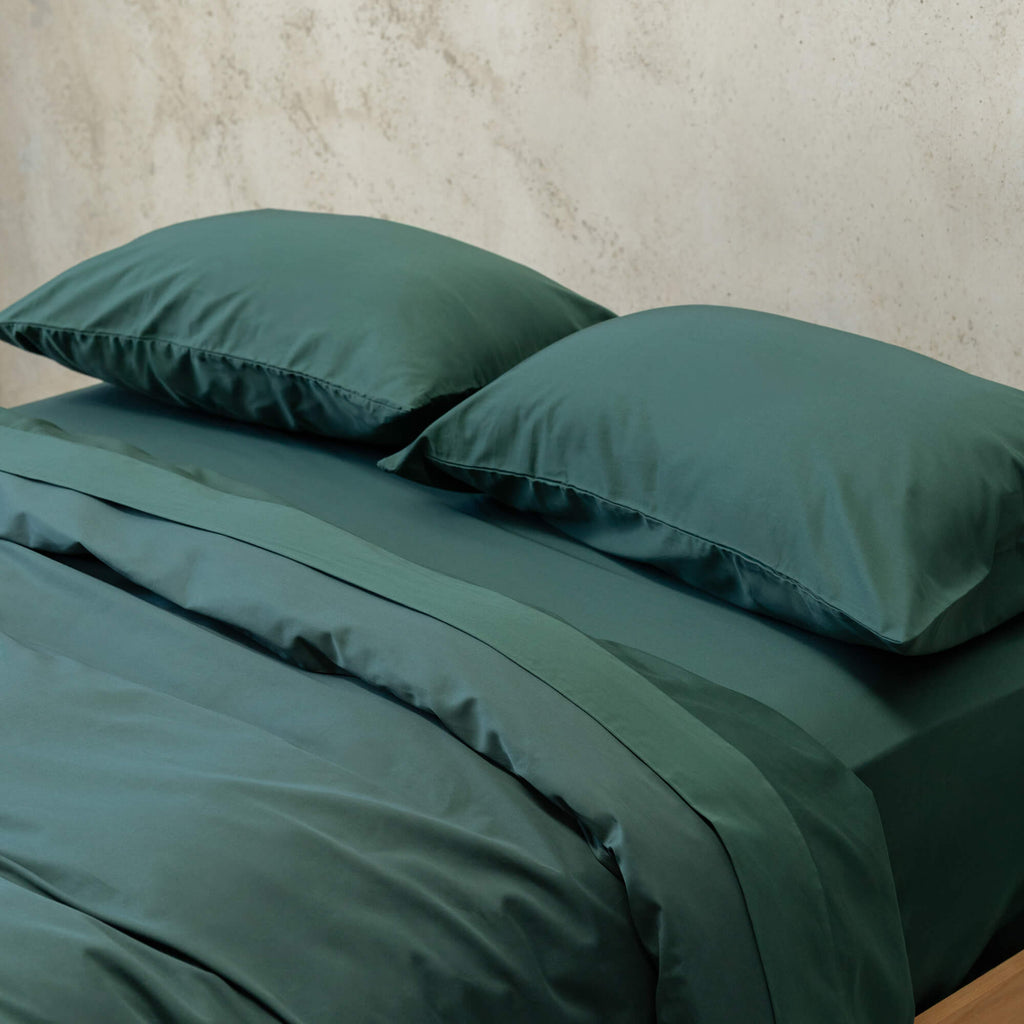 Green bedspread and pillows on a bed with concrete in the background