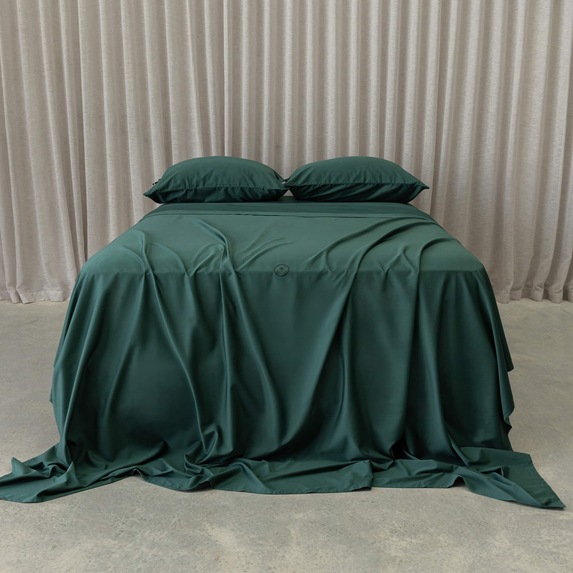 Green bedspread on a bed with matching pillows against a beige curtain background
