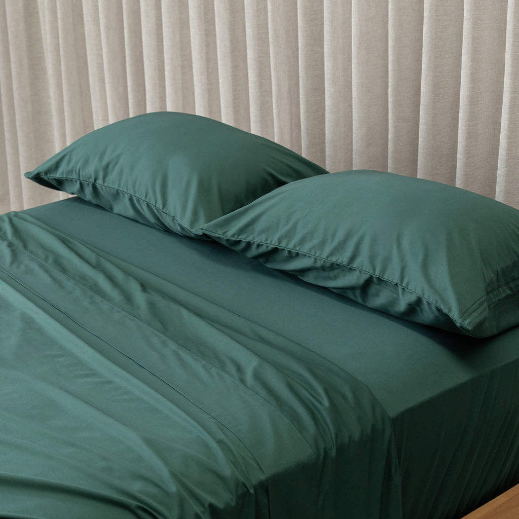 Green bedspread on a bed with white pillows against a beige curtain background