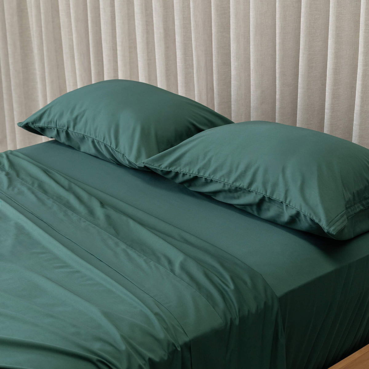 Green bedspread on a bed with white pillows against a beige curtain background