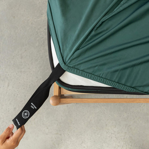 Person adjusting a green fitted sheet with a black strap on a gray surface
