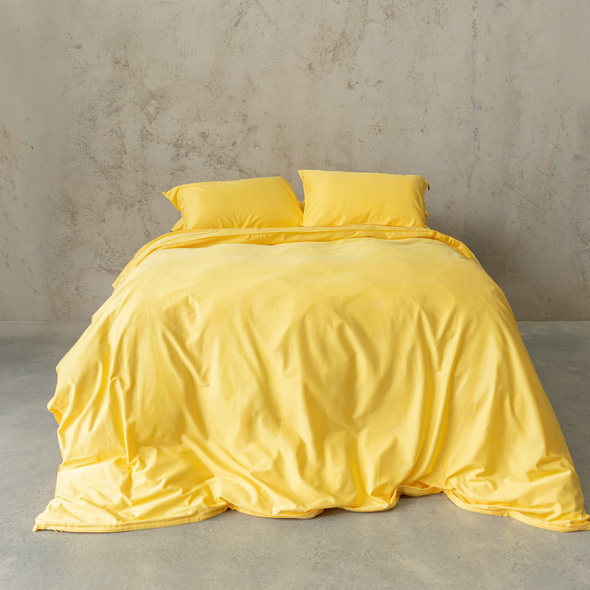 Bright yellow duvet cover set on a bed, against a neutral concrete look backdrop.